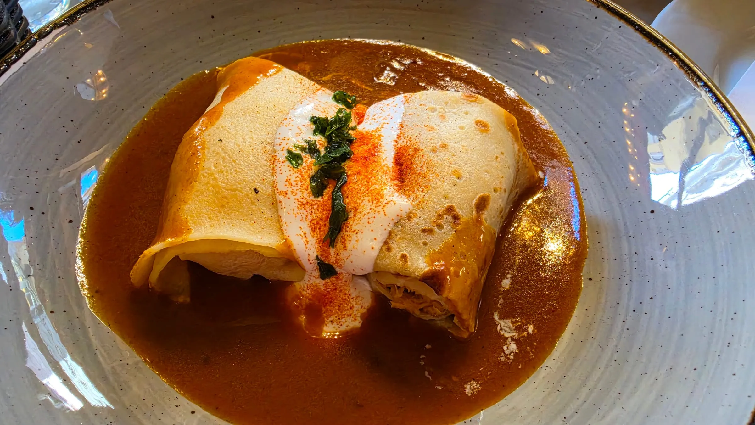 Dve slané palacinky plnené mäsom v hlbokom sivom tanieri, zaliate oranžovou paprikovou omáčkou, navrchu kyslá smotana, mletá paprika a petržlenová vňať