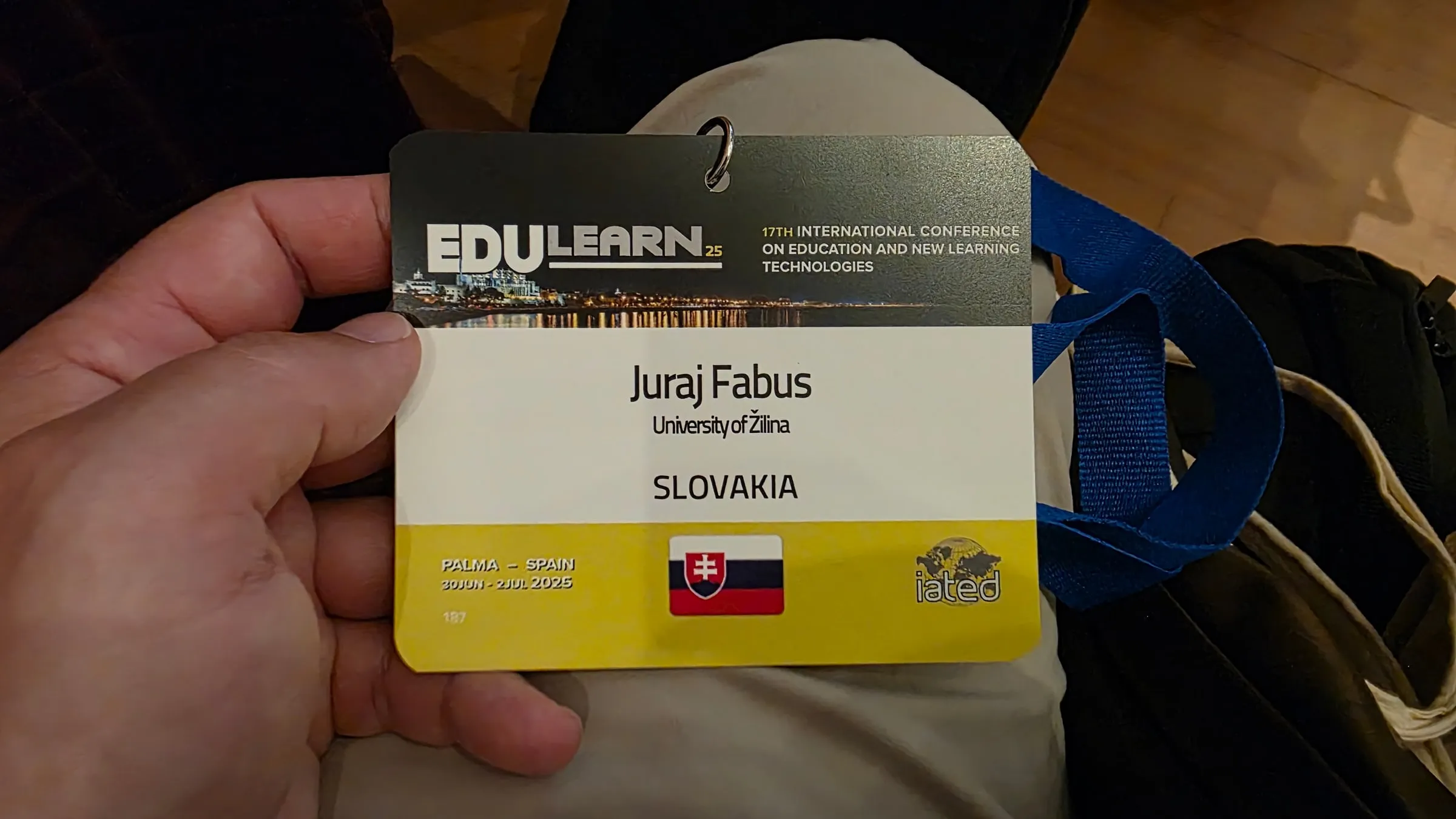 A hand holds an EDULEARN25 conference badge with the name Juraj Fabus, University of Žilina, a Slovak flag and a blue lanyard; a night photo of Palma in the header